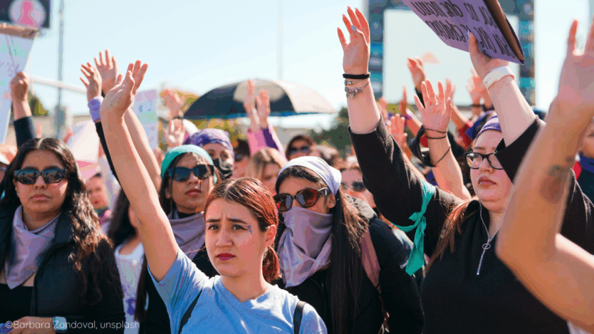 A group of young women raising their hands in the air at a protest.